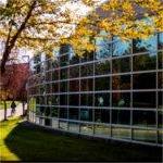 A bicyclist rides by a mirrored building.